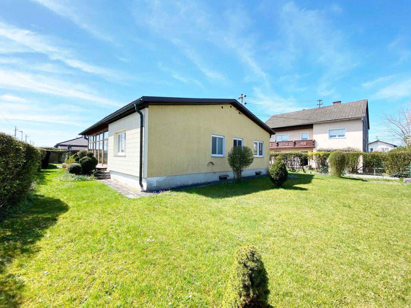 Gelbes Einfamilienhaus mit großem, sonnigem Garten und blauen Himmel.