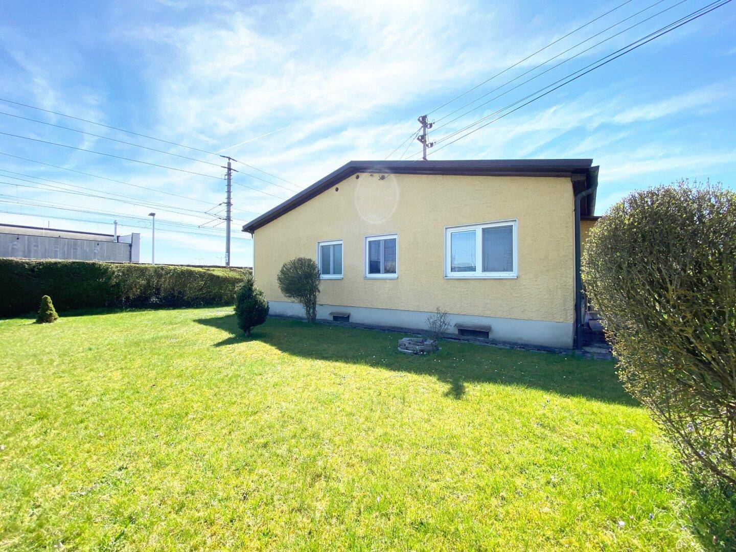 Rückseite des gelben Einfamilienhauses mit großem Garten und Hecke.