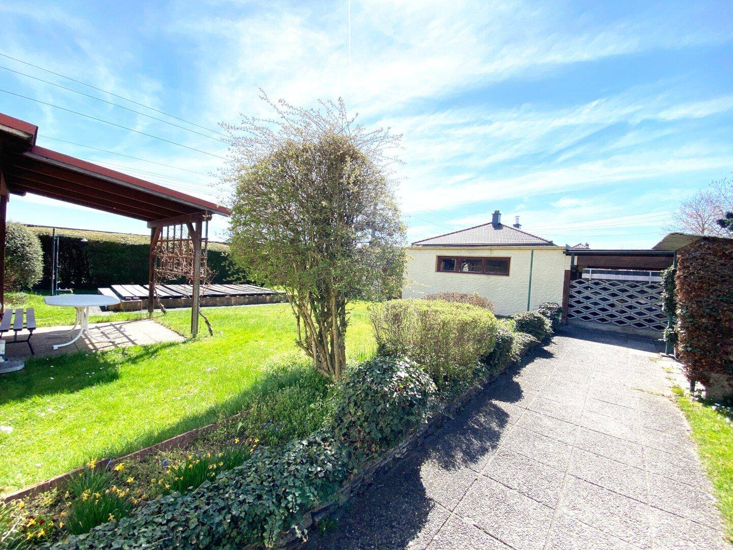 Einfahrt zum Haus mit gepflegtem Garten und weiteren Gebäuden im Hintergrund.