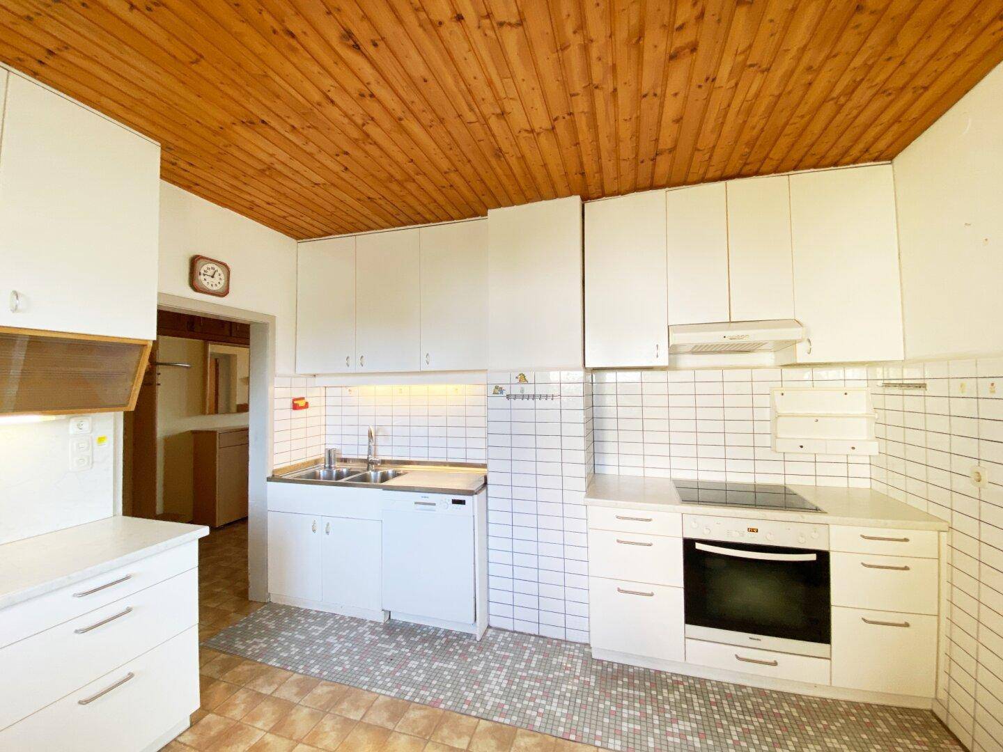 Helle Küche mit weißen Schränken, Fliesen und einer Holzdecke im Landhausstil.