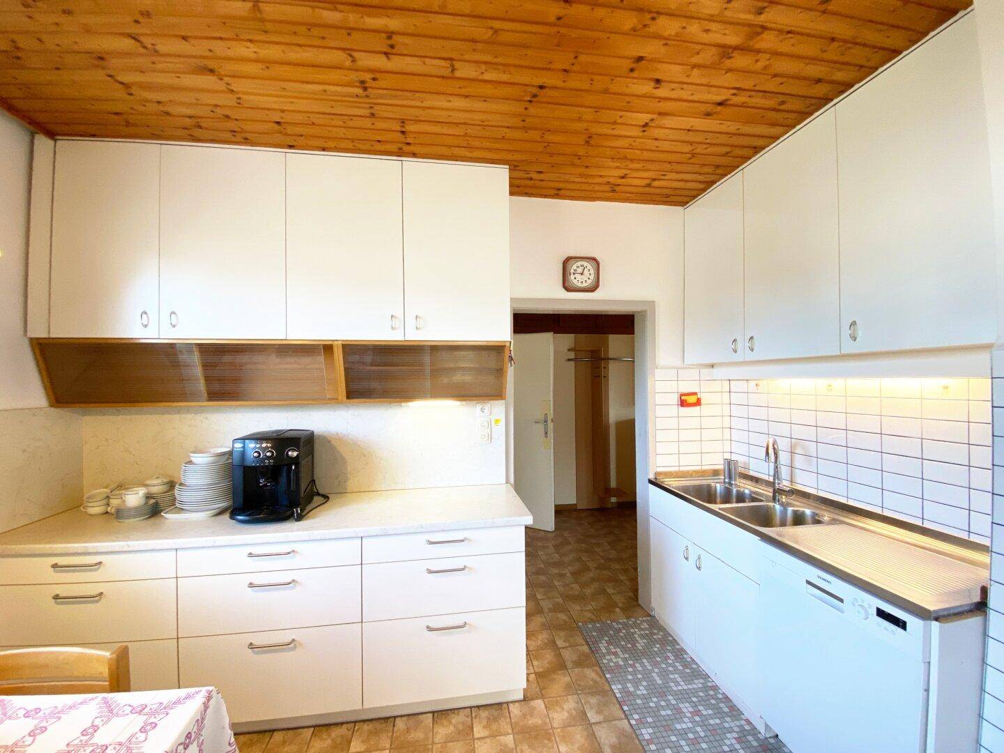 Gemütliche Küche mit weißen Einbauschränken, Holzdecke und Kaffeemaschine.