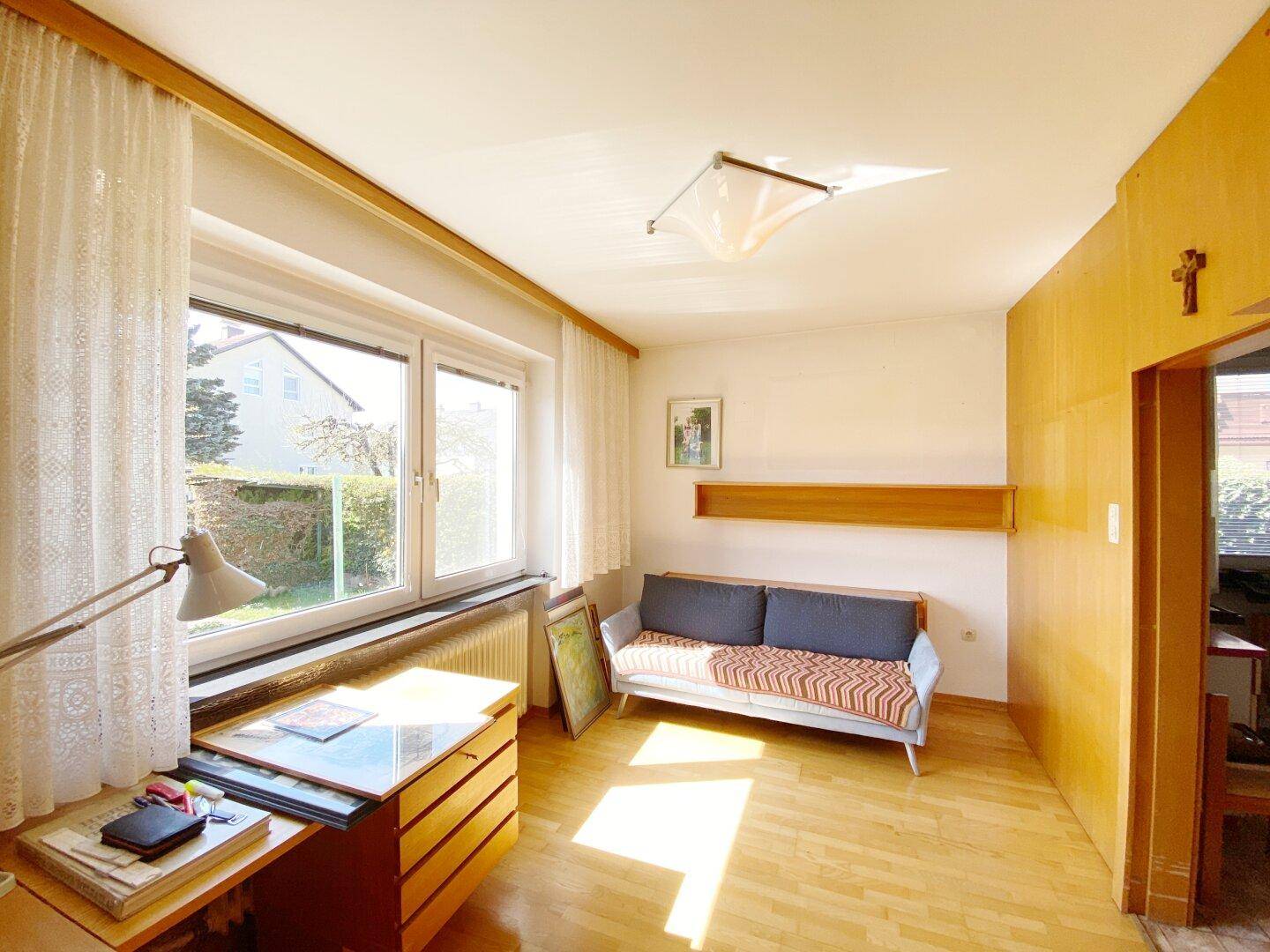 Helles Arbeitszimmer mit großem Fenster, Schreibtisch und Parkettboden.