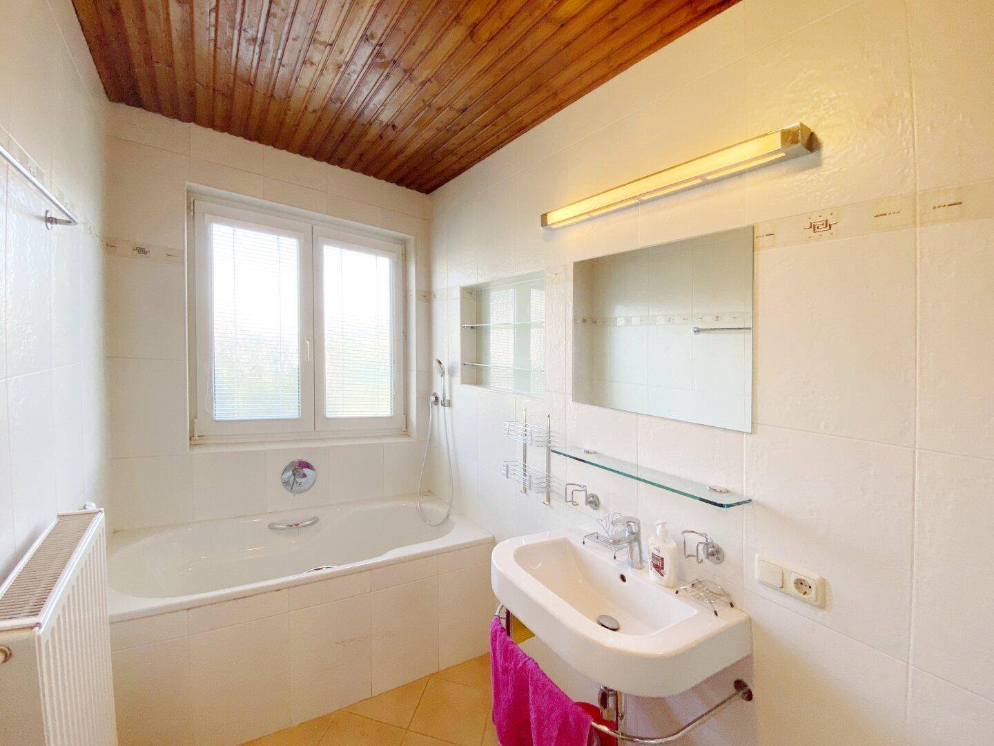 Badezimmer mit Badewanne, Waschbecken, Fenster und Holzdecke.