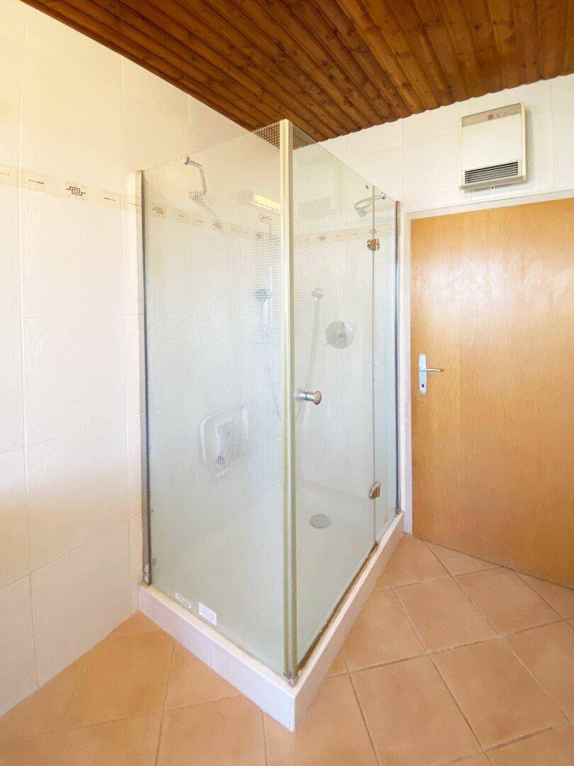 Badezimmer mit Duschkabine, Fliesenboden und Holzdecke.