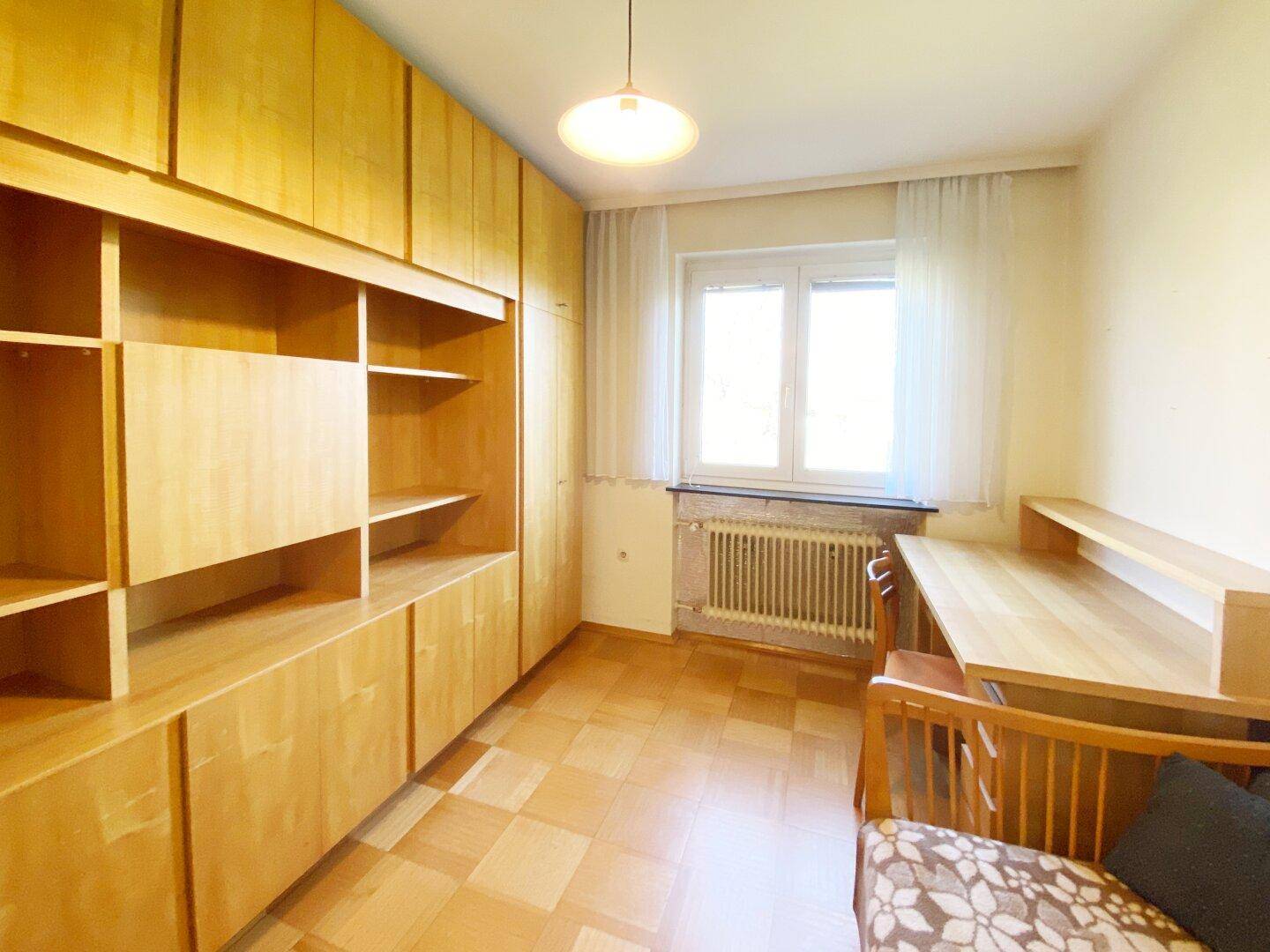 Zimmer mit Holzschränken, Schreibtisch und Fenster, ideal als Kinder- oder Gästezimmer.