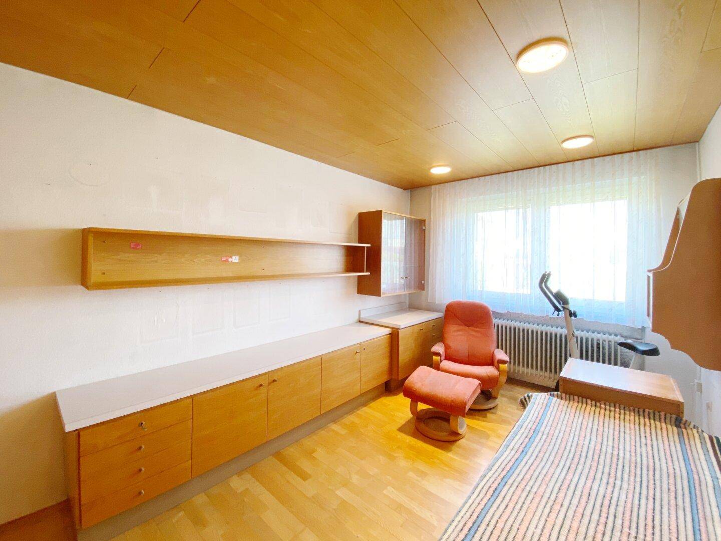 Geräumiges Zimmer mit Holzmöbeln, Parkettboden und großem Fenster.