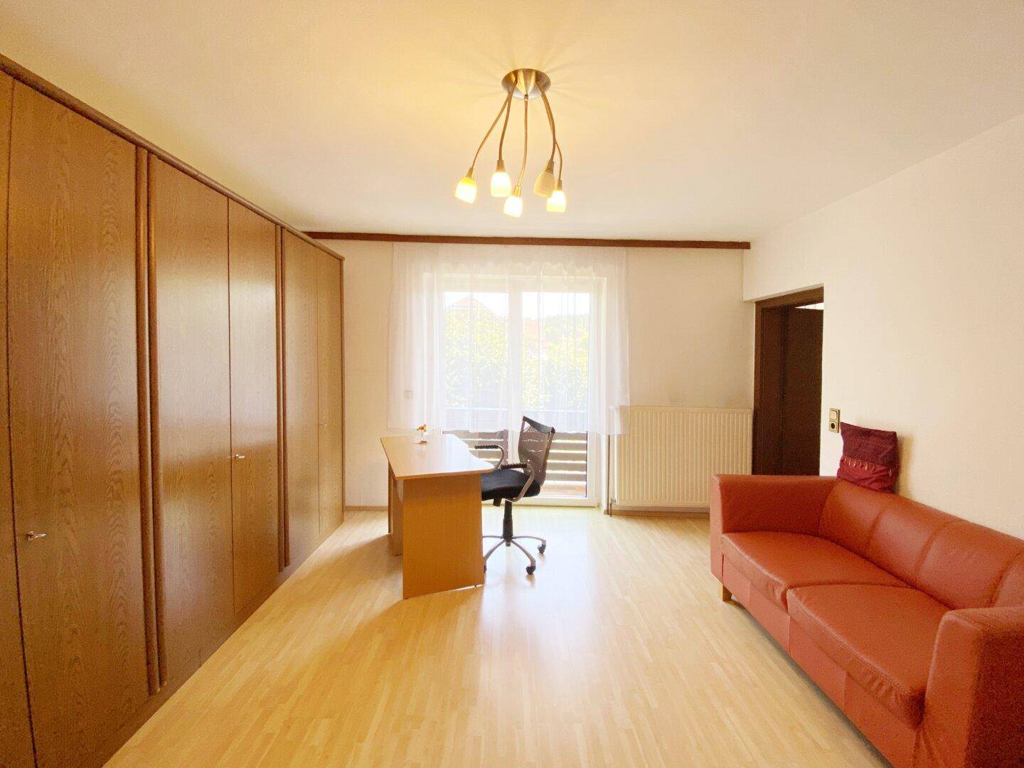 Geräumiges Zimmer mit Holzfußboden, Einbauschränken, Schreibtisch und Balkonzugang.