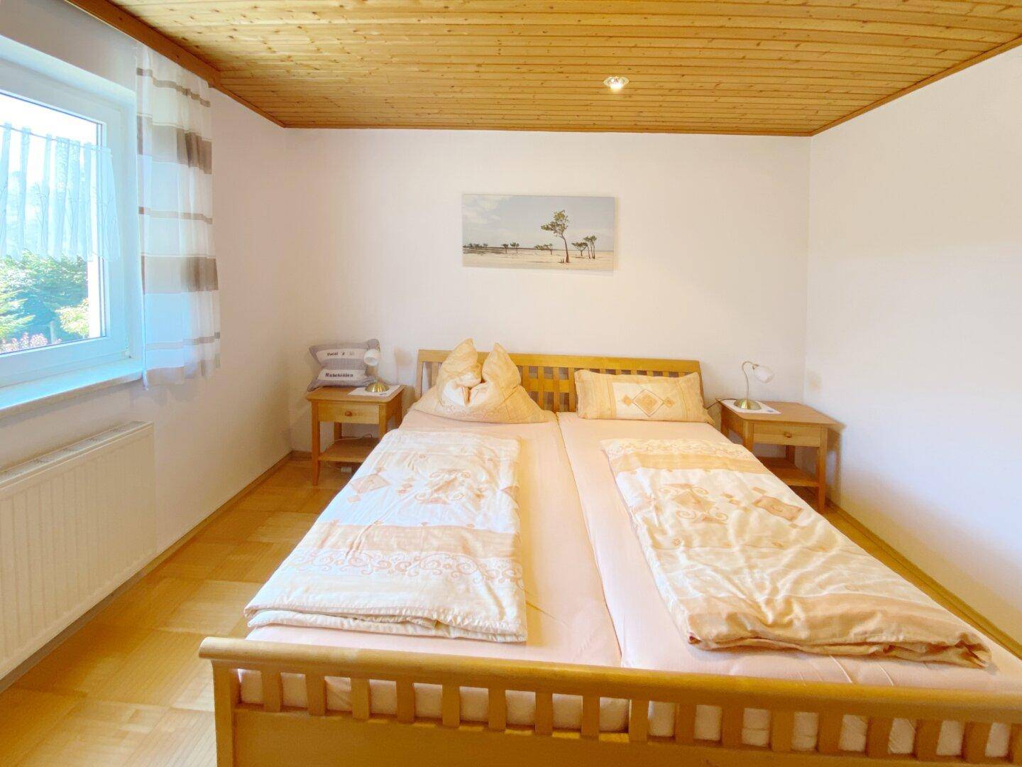 Schlafzimmer mit Holzlatten-Decke, Doppelbett, Nachttischen und Fenster mit Ausblick.