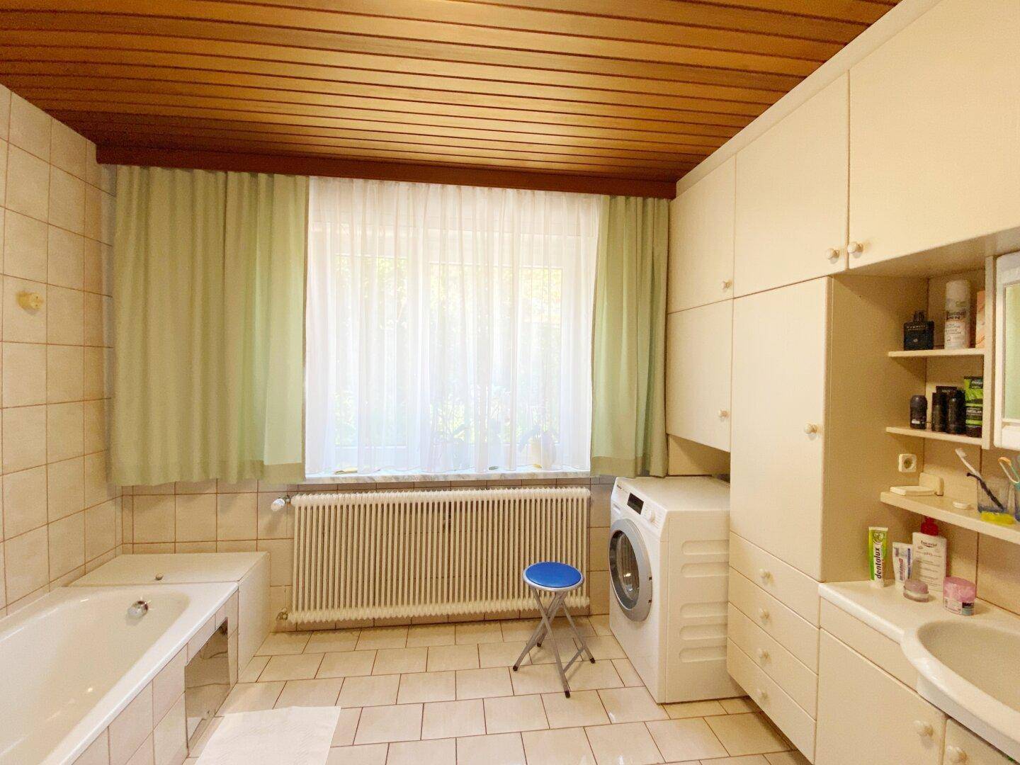 Badezimmer mit Badewanne, Waschmaschine, Waschbecken und Holzlatten-Decke.