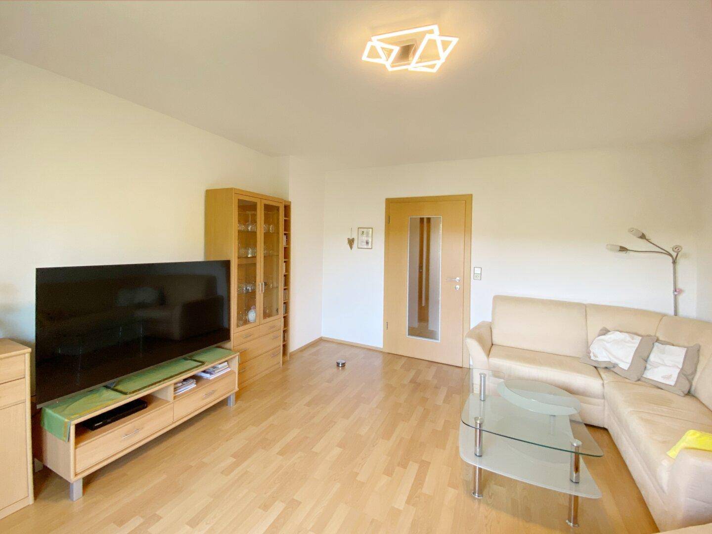 Helles Wohnzimmer mit beigem Sofa, TV-Möbeln, Vitrine und Holzfußboden.