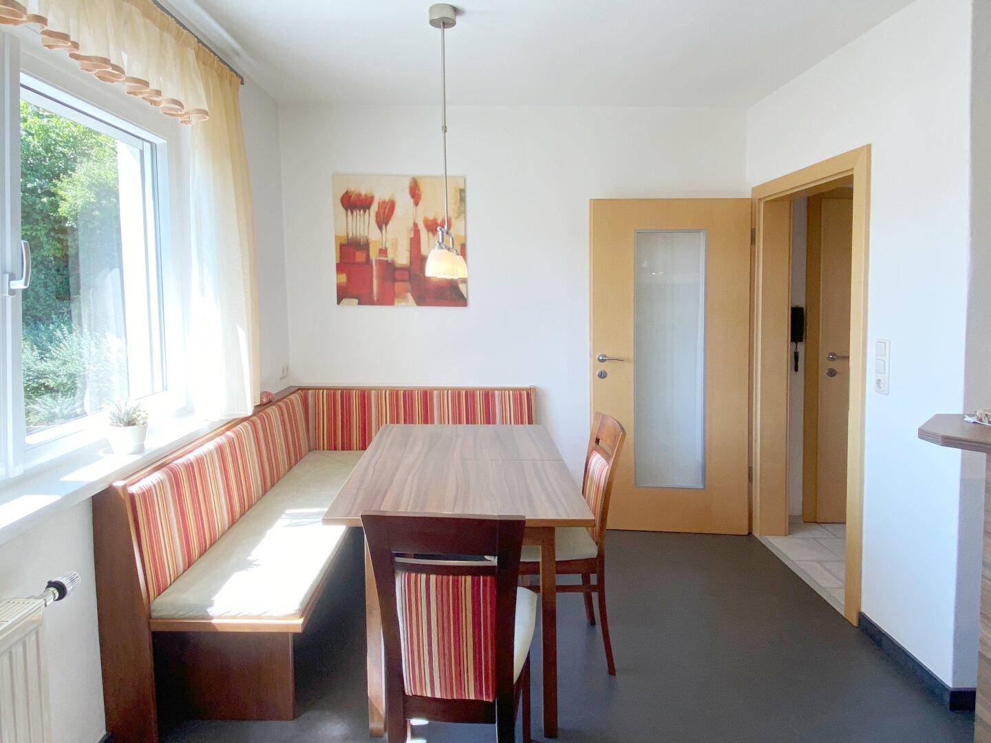 Heller Essbereich mit eingebauter Sitzbank, Esstisch und Fenster mit Blick ins Grüne.