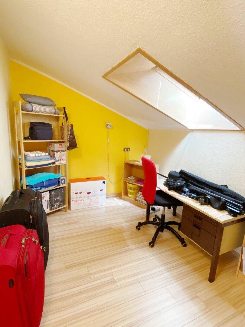 Arbeitszimmer im Dachgeschoss mit Dachschräge, Dachfenster, gelber Wand und Schreibtisch.