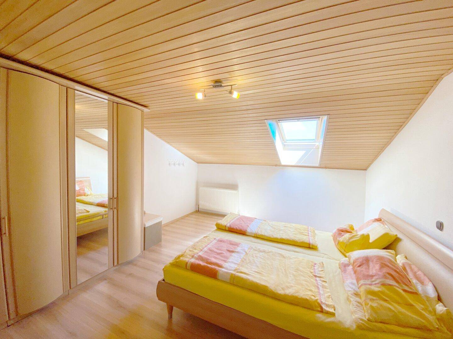 Schlafzimmer im Dachgeschoss mit Dachschräge, Holzlatten-Decke, Dachfenster und Holzfußboden.