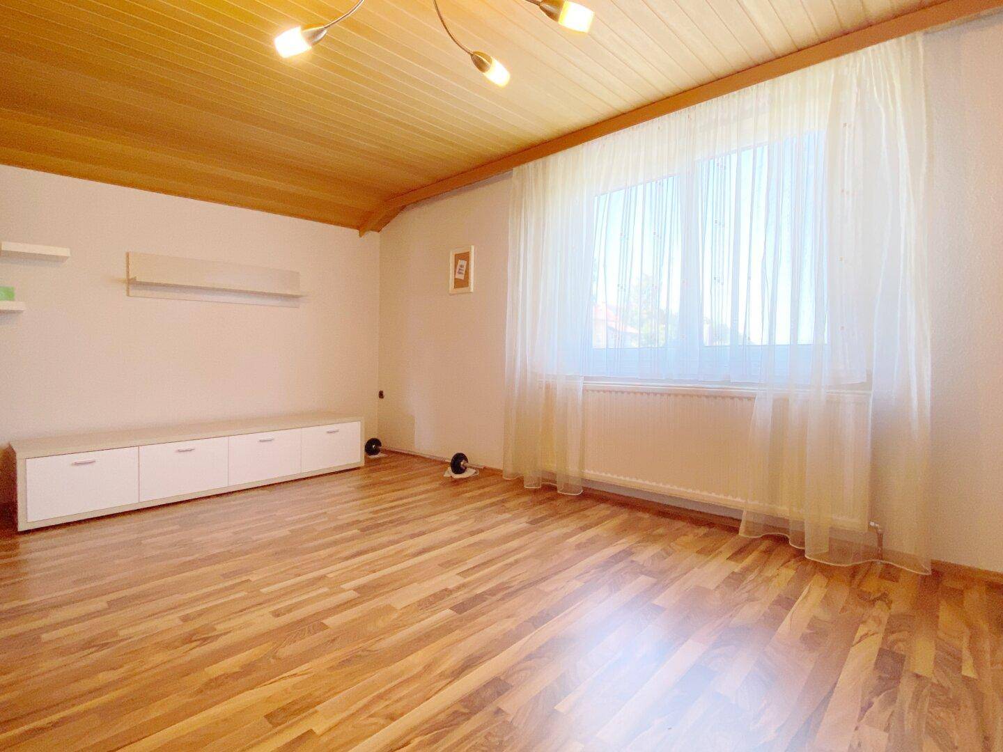 Heller Raum mit Holzfußboden, Fenster, weißer Medienkonsole und Holzlatten-Decke.
