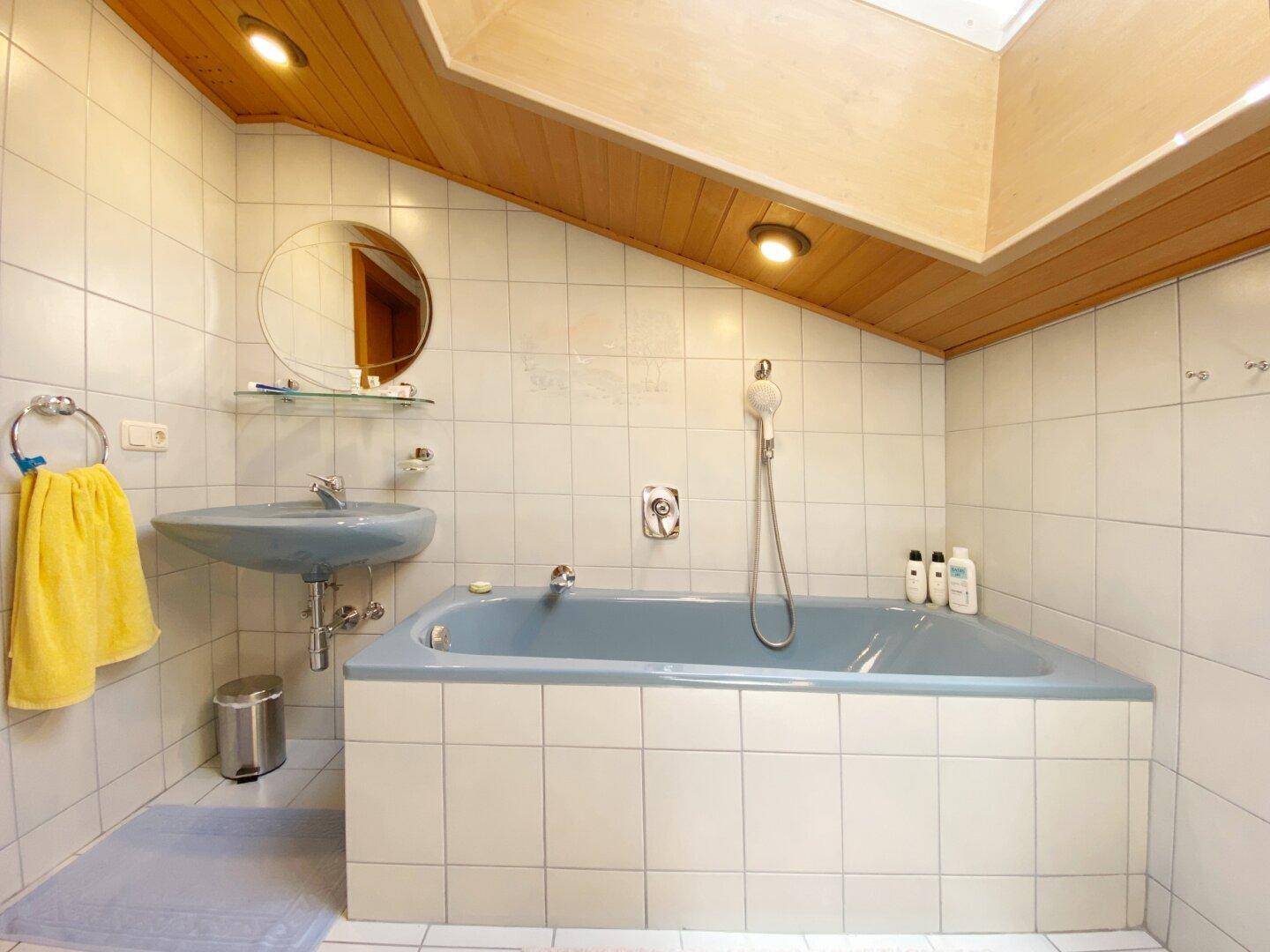 Badezimmer im Dachgeschoss mit Dachschräge, Dachfenster, Eckbadewanne und blauer Keramik.