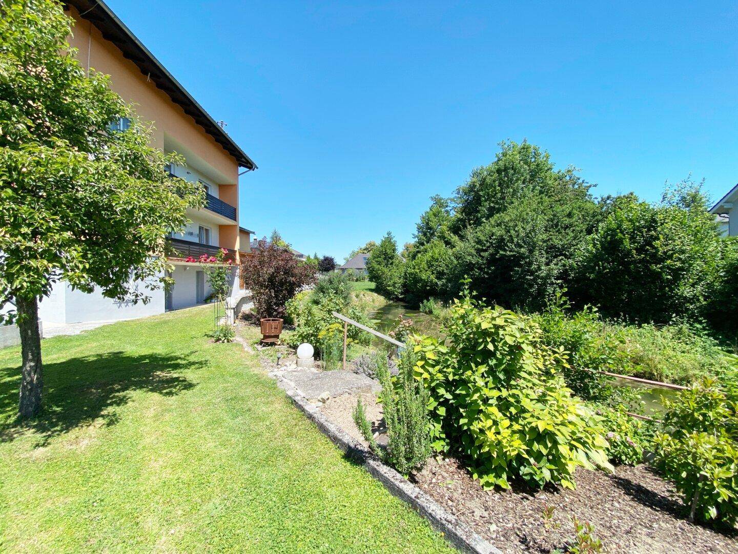 Seitenansicht des Hauses mit gepflegtem Gartenbereich entlang des natürlichen Bachlaufs.