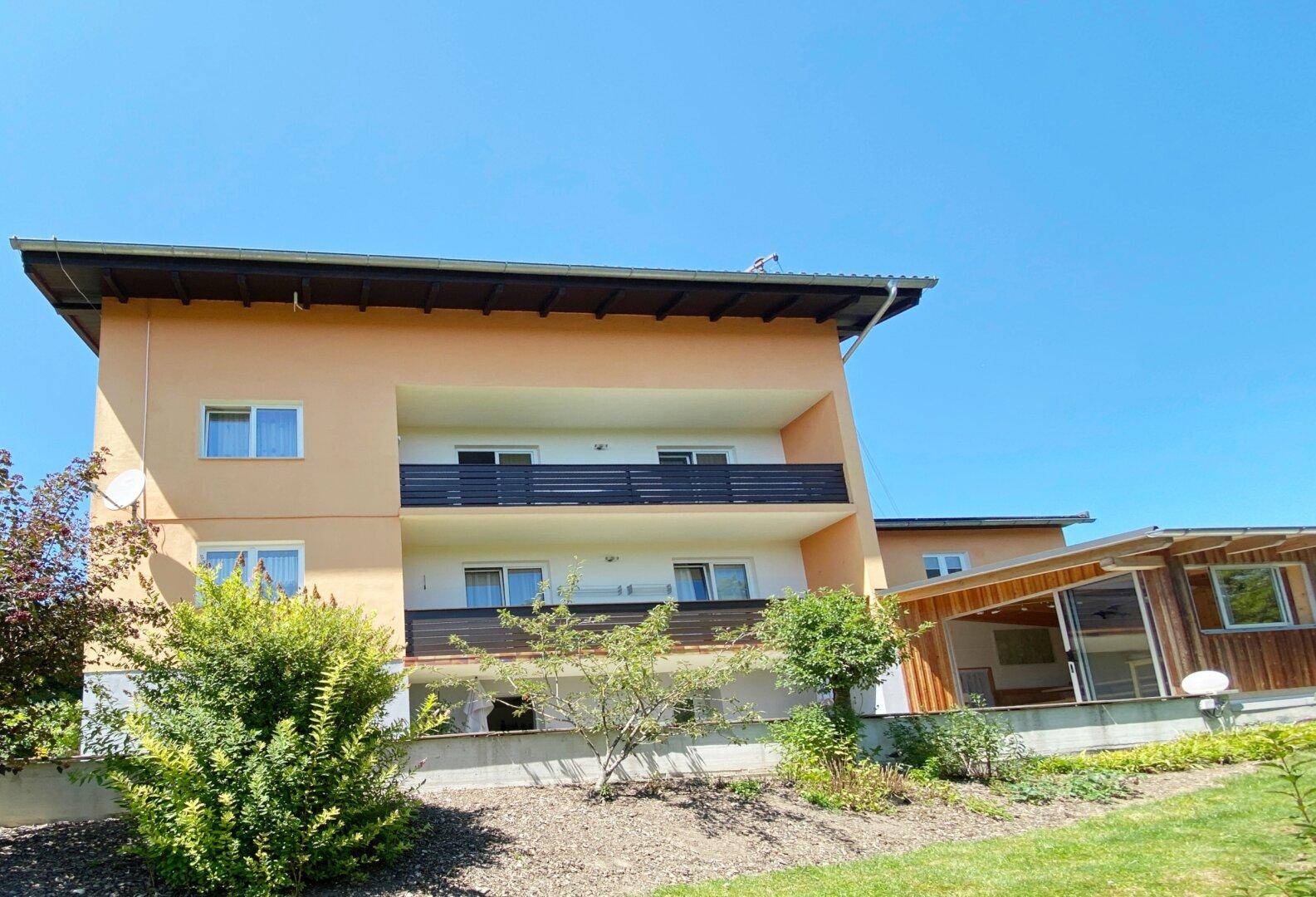Ansicht des Gebäudes mit peachfarbener Fassade, Balkonen und grüner Umgebung unter blauem Himmel.