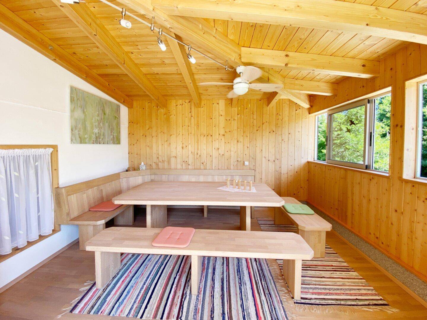 Gemütlicher Essbereich im alpinen Stil mit viel Holz, großen Fenstern und Deckenventilator.