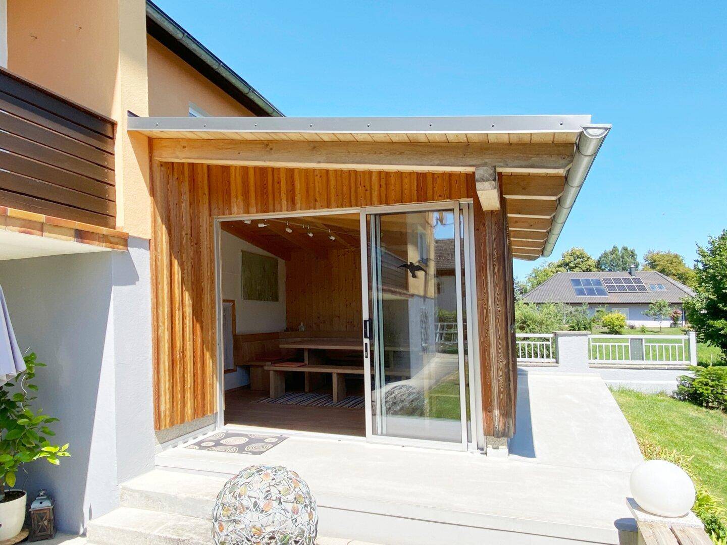 Außenansicht eines Holz-Anbaus mit großen Glasschiebetüren, der einen Wellnessbereich beherbergt.
