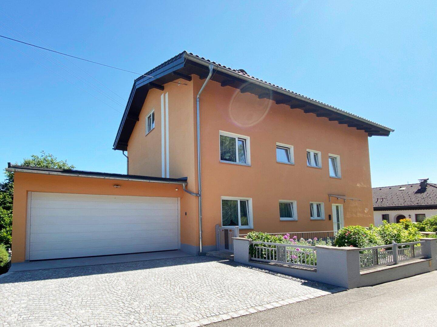 Vorderansicht des Hauses mit peachfarbener Fassade, integrierter Garage und gepflasterter Auffahrt.