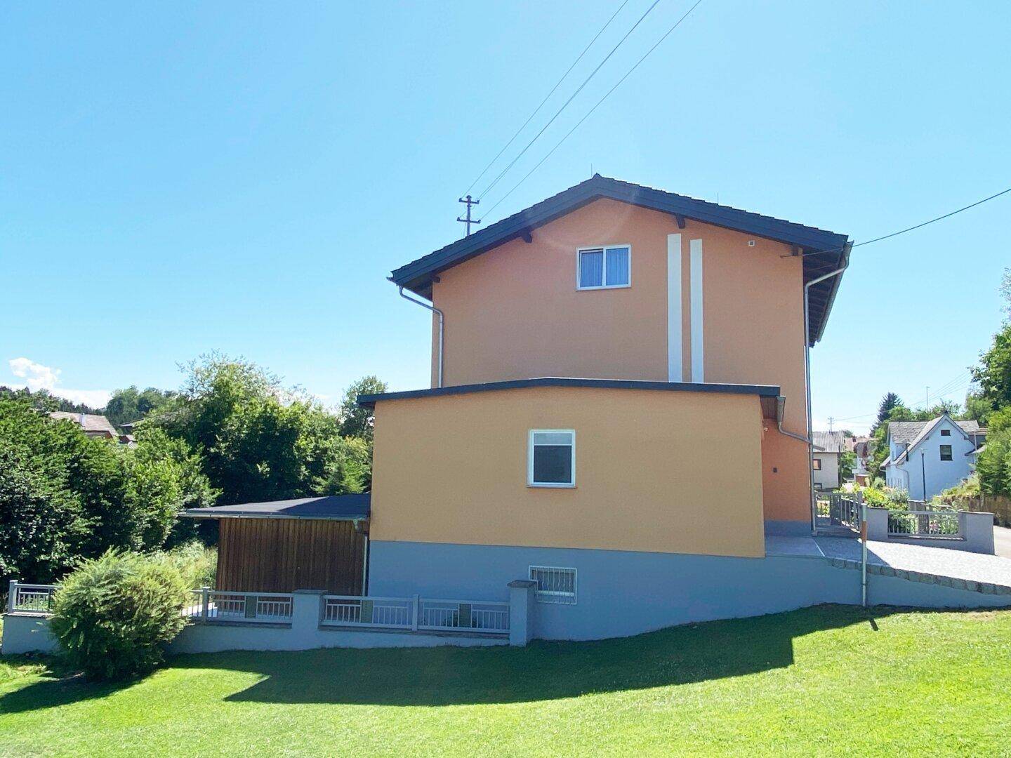 Rückansicht des Gebäudes mit peachfarbener Fassade, Holzverkleidung im Untergeschoss und weitläufigem Rasen.