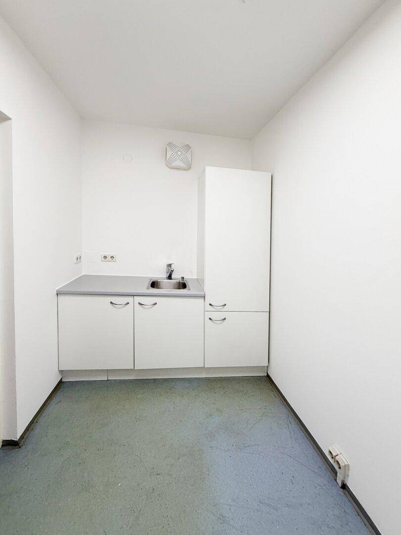 Kleine Teeküche mit weißer Küchenzeile, Spülbecken und Abluftventilator, ideal für kurze Pausen.