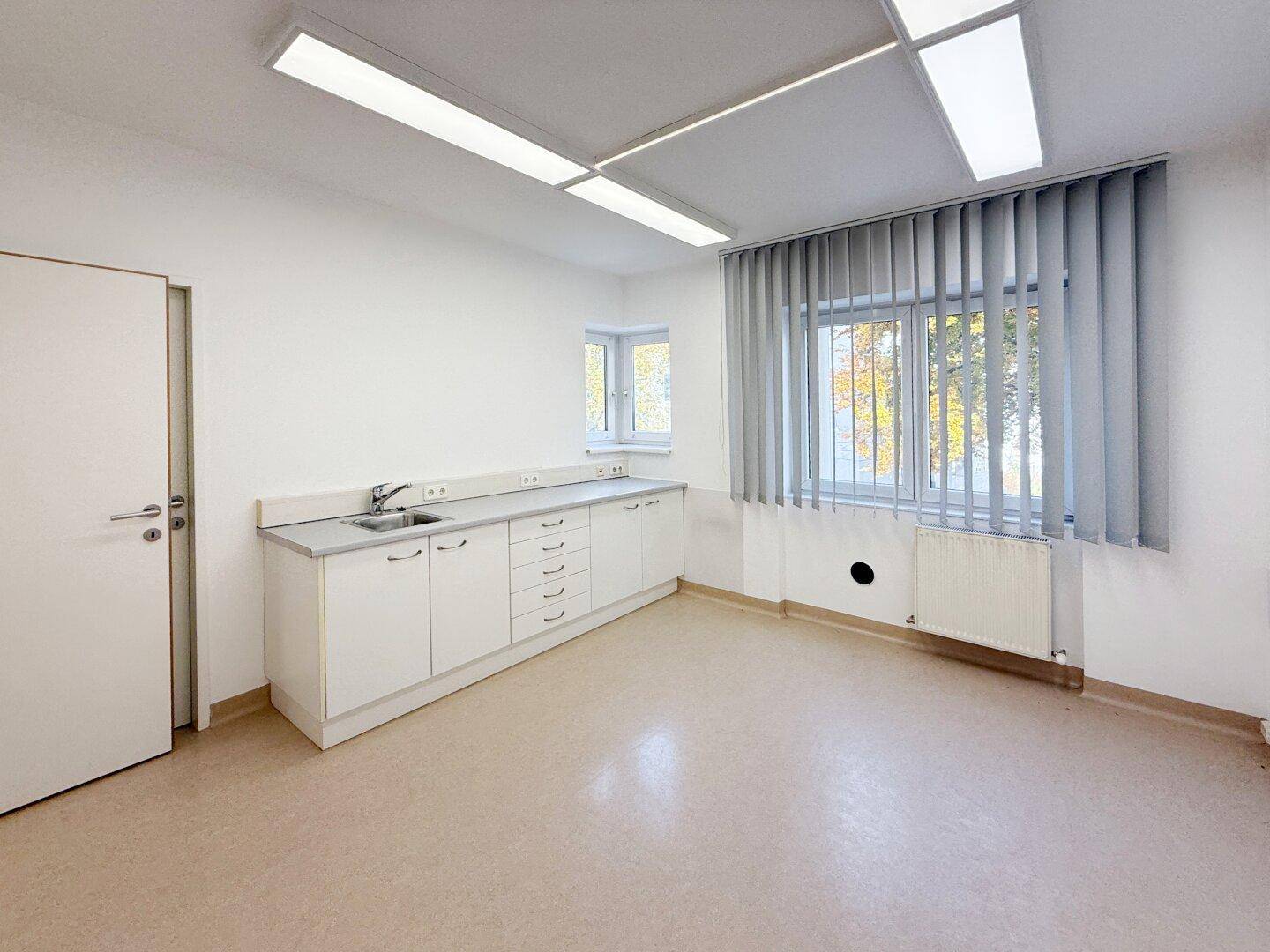 Geräumiges Büro mit langer weißer Arbeitsplatte, Spülbecken und großen Fenstern, die viel Tageslicht hereinlassen.