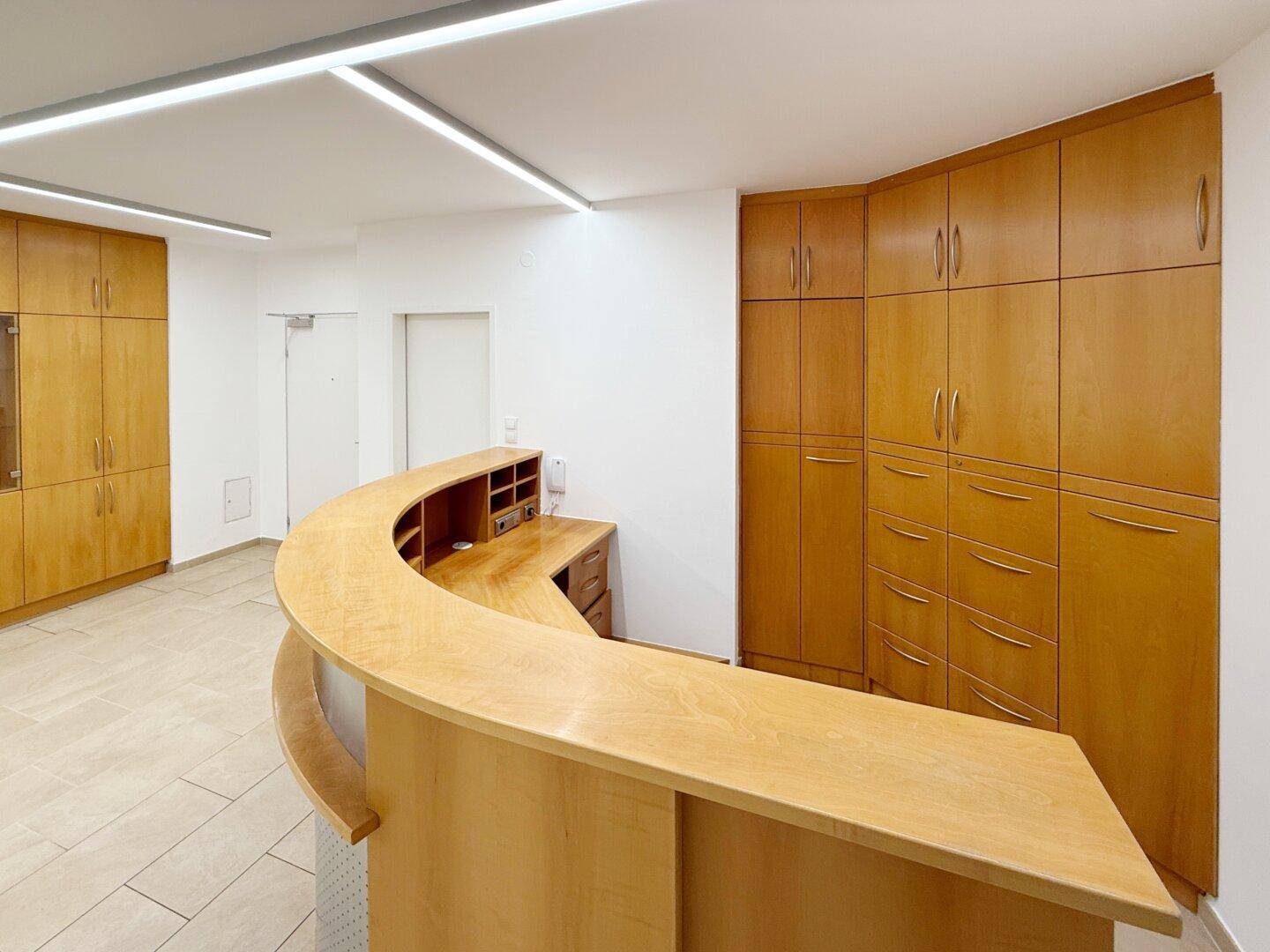 Heller Empfangsbereich mit geschwungener Holztheke und integrierten Holzschränken, ideal für Büroräume.