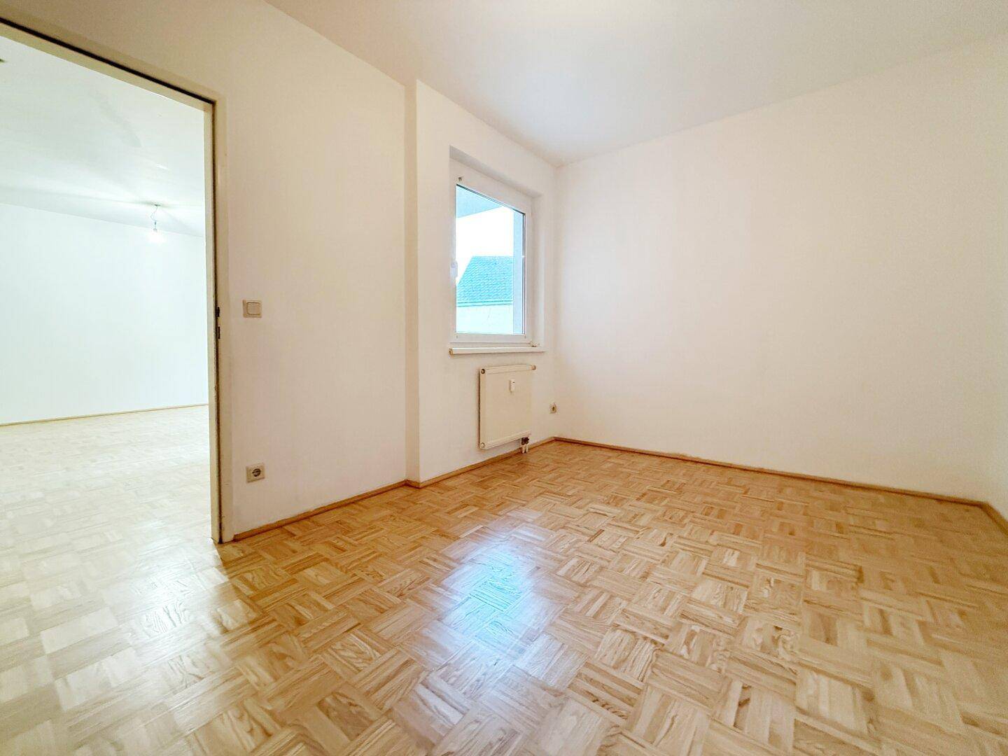 Helles Zimmer mit Parkettboden und einem Fenster, ideal als Schlaf- oder Arbeitszimmer.