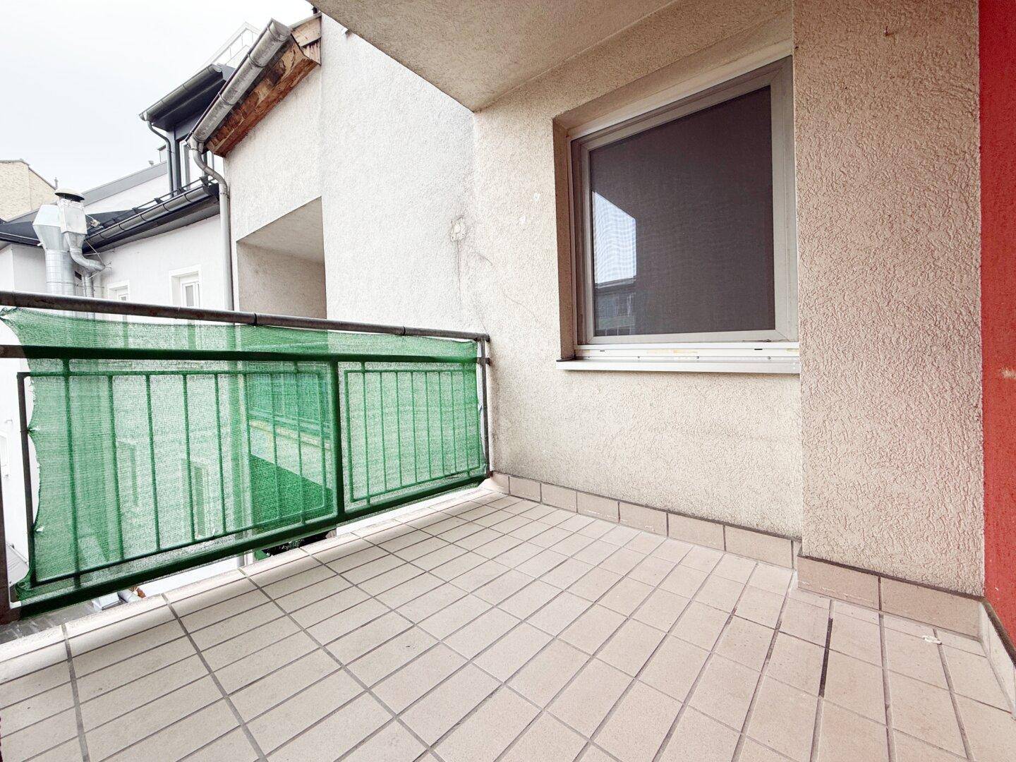 Kleiner Balkon mit Fliesenboden und grüner Sichtschutzverkleidung.
