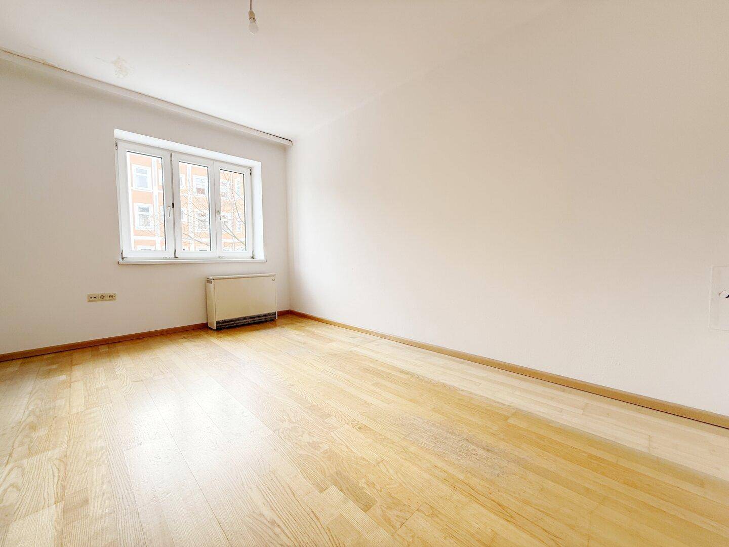 Lichtdurchfluteter Raum mit Parkett und Heizkörper unter dem Fenster.