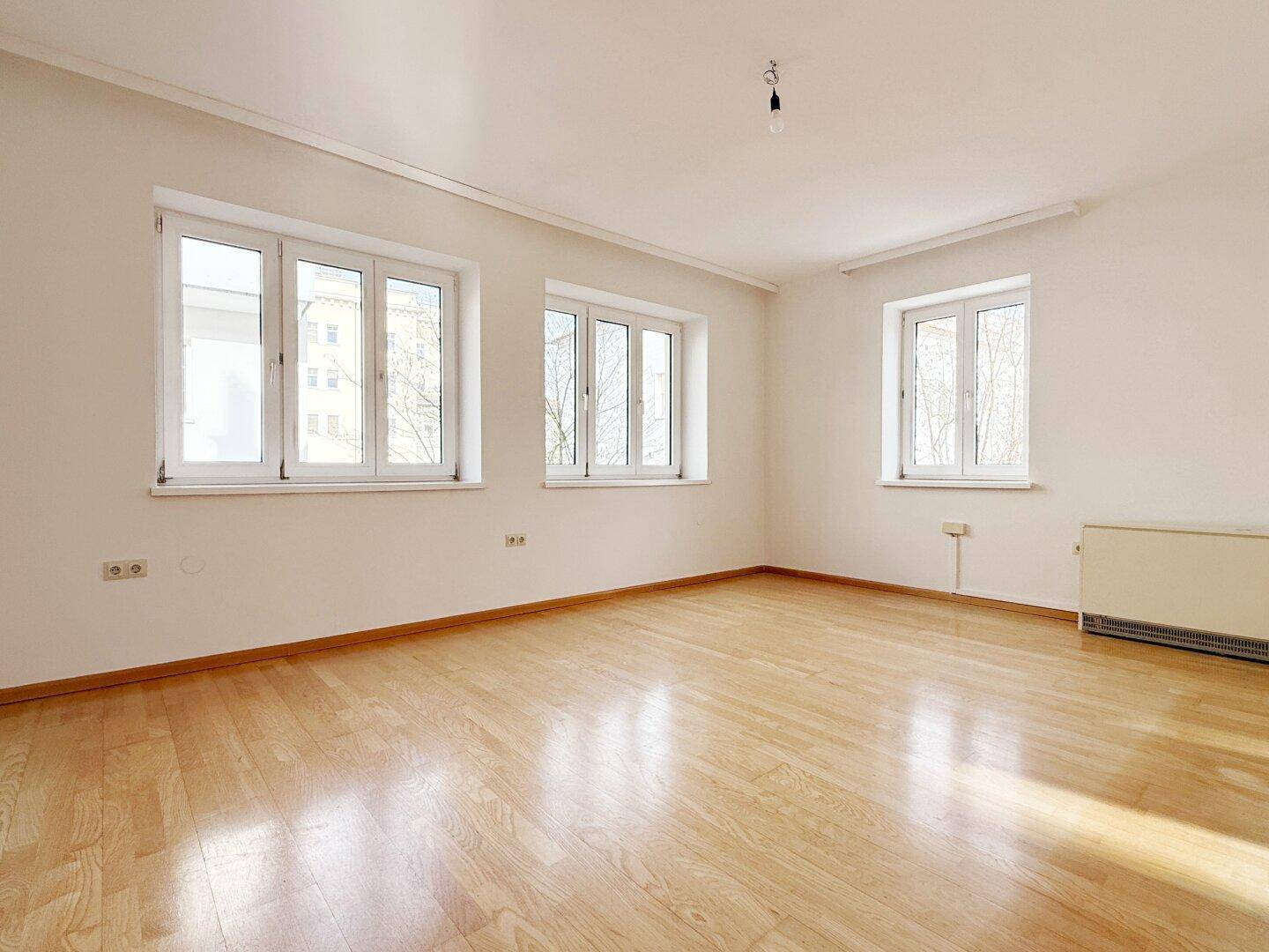 Heller Wohnraum mit Parkettboden und mehreren Fenstern für viel Tageslicht.