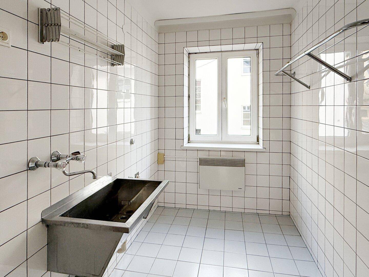 Praktischer Hauswirtschaftsraum mit großem Waschbecken und weißen Fliesen.