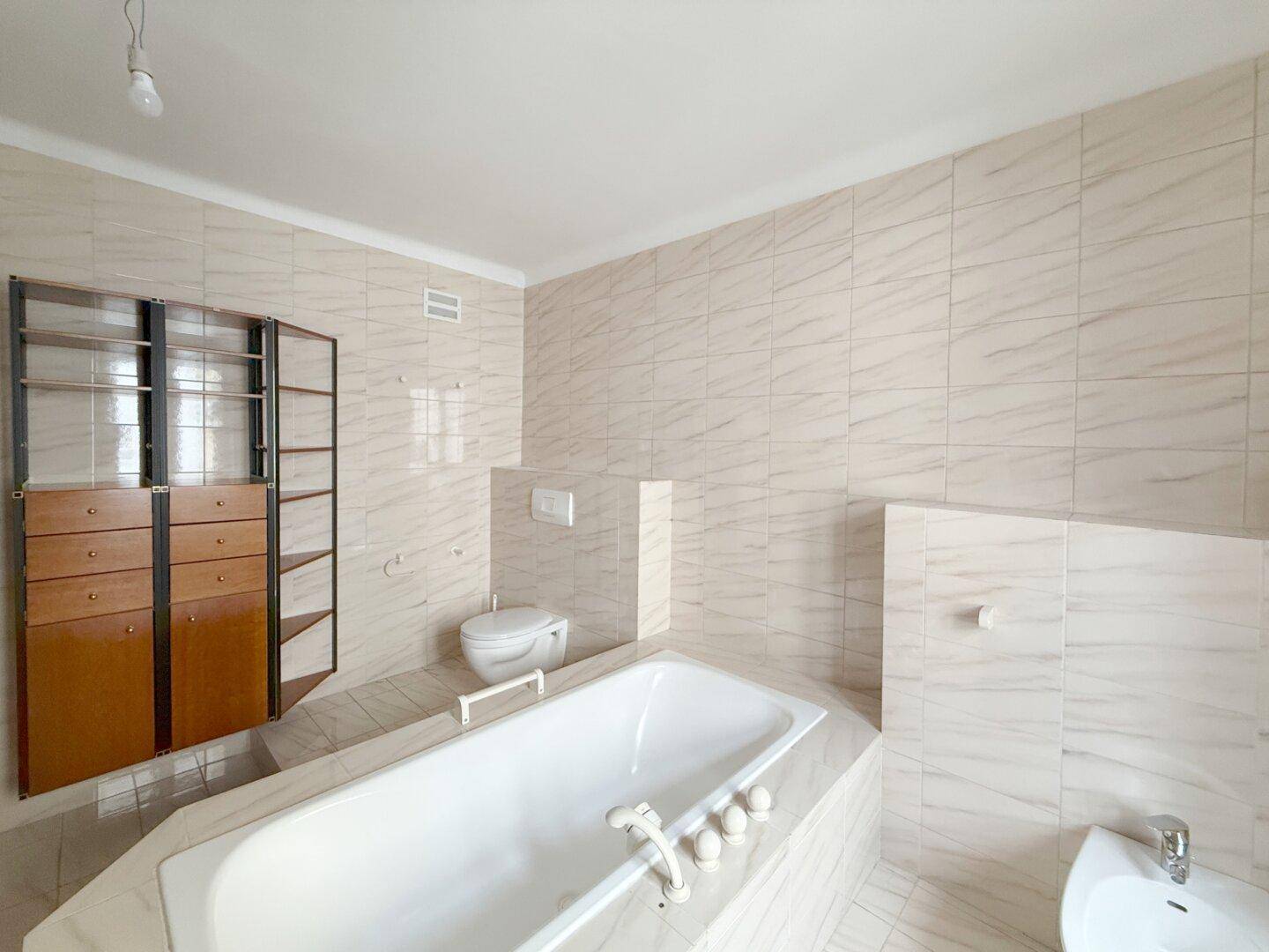 Badezimmer mit Badewanne, wandhängendem WC und Bidet in hellen Fliesen.