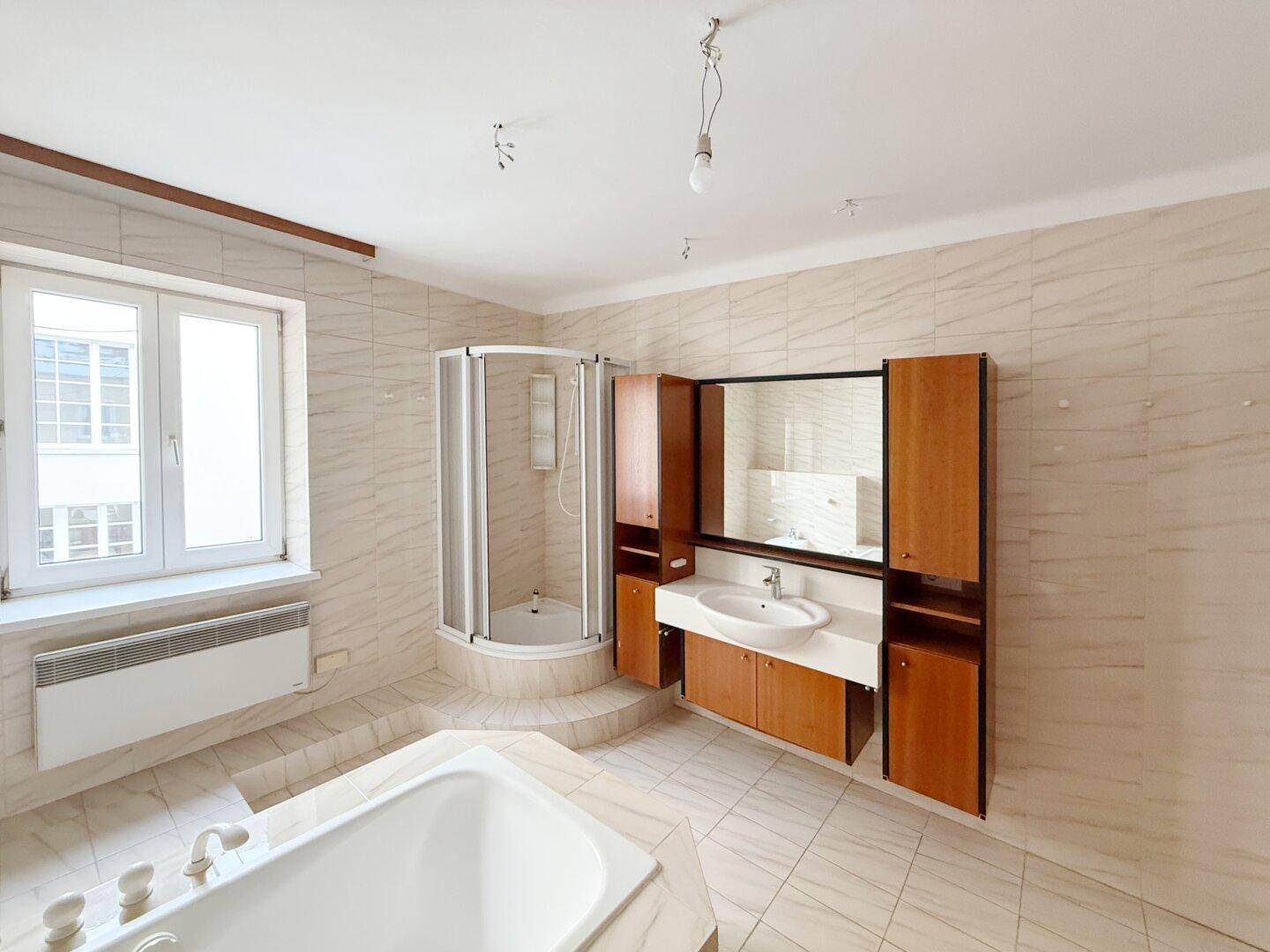 Helles Badezimmer mit Badewanne, Eckdusche, Waschtisch und Fenster.