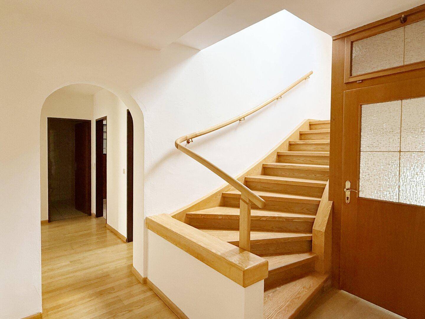 Heller Eingangsbereich mit Holztreppe und Zugang zu weiteren Räumen.