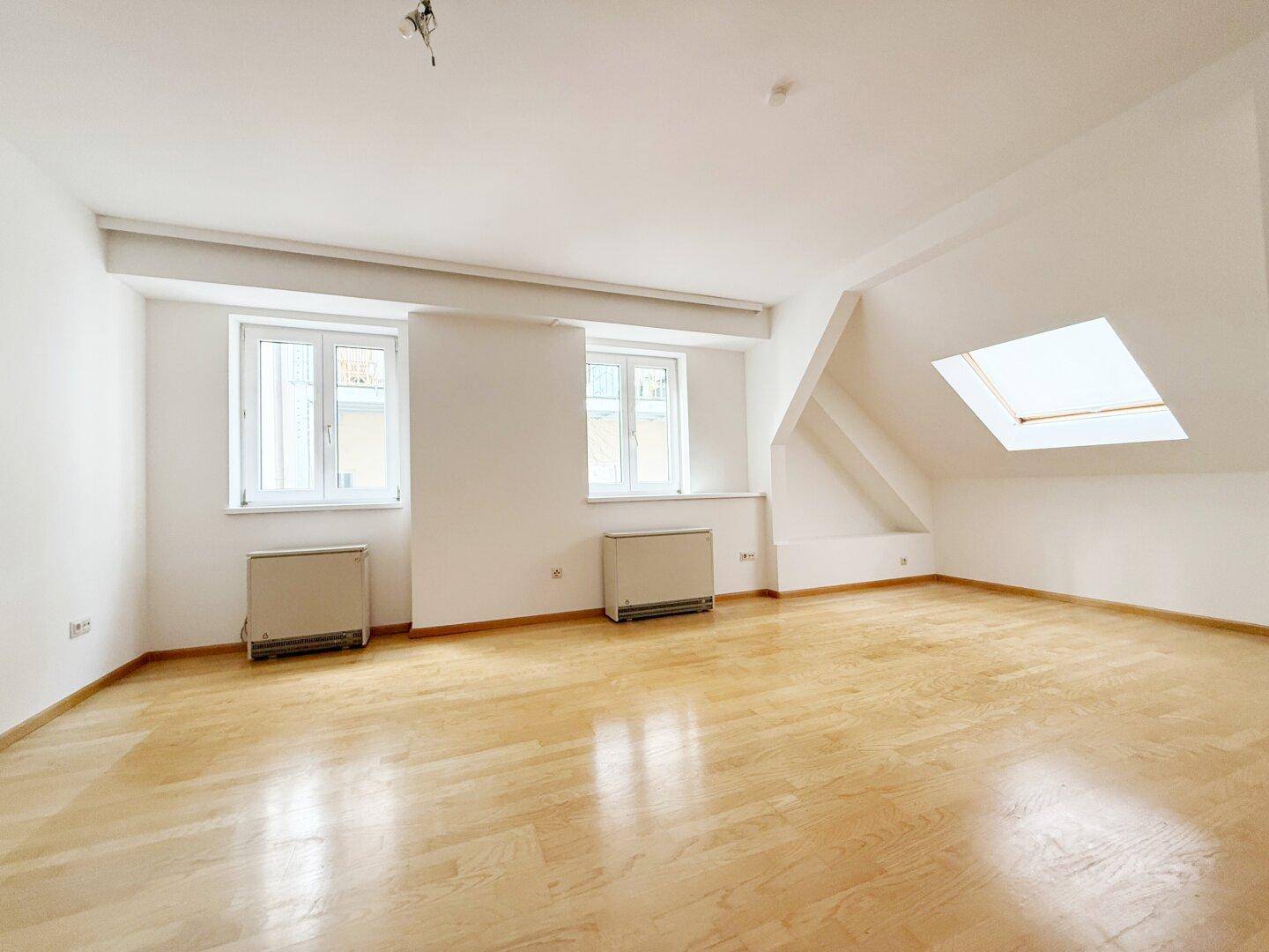 Geräumiger Dachraum mit Parkettboden, Dachschräge und Dachfenster.