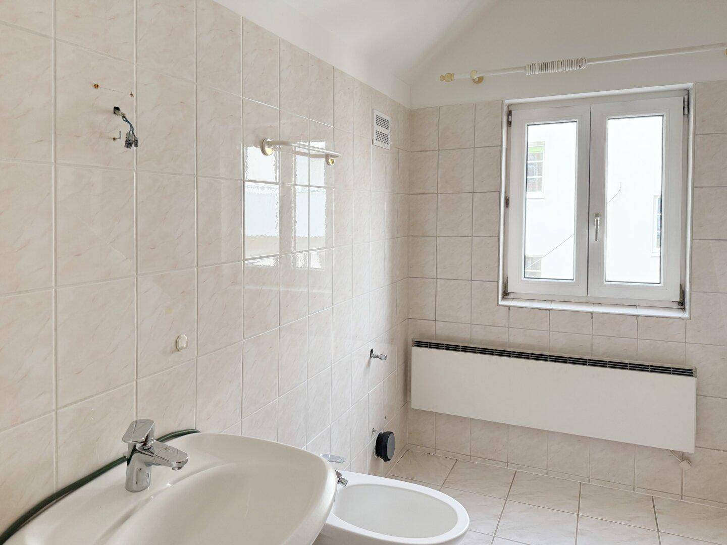 Badezimmer mit Waschbecken, Toilette und Fenster für natürliche Belüftung.