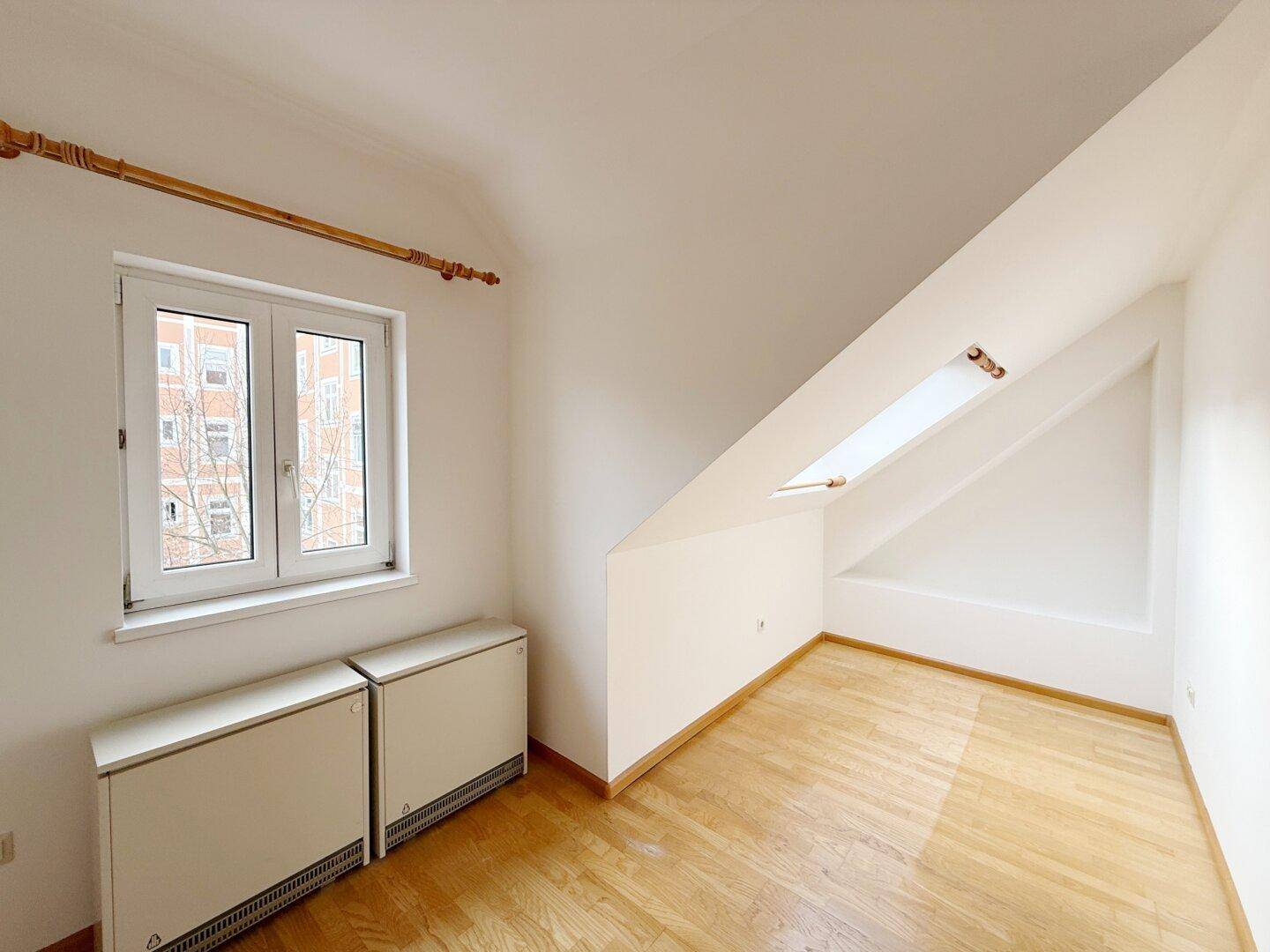Heller Dachraum mit Parkettboden, Dachschräge und einem Dachfenster.