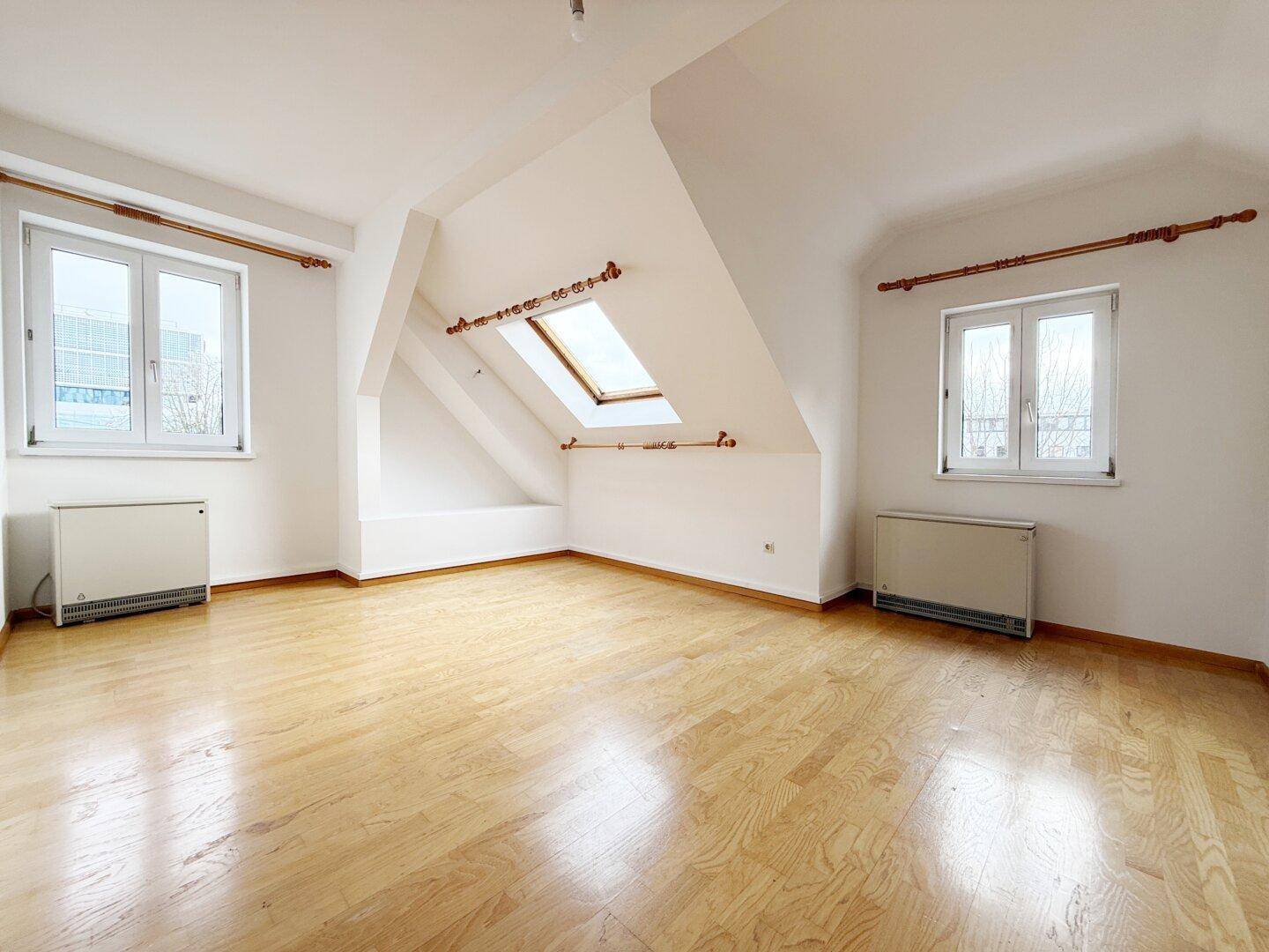 Lichtdurchfluteter Dachraum mit Parkett, Dachschräge und Dachfenster.