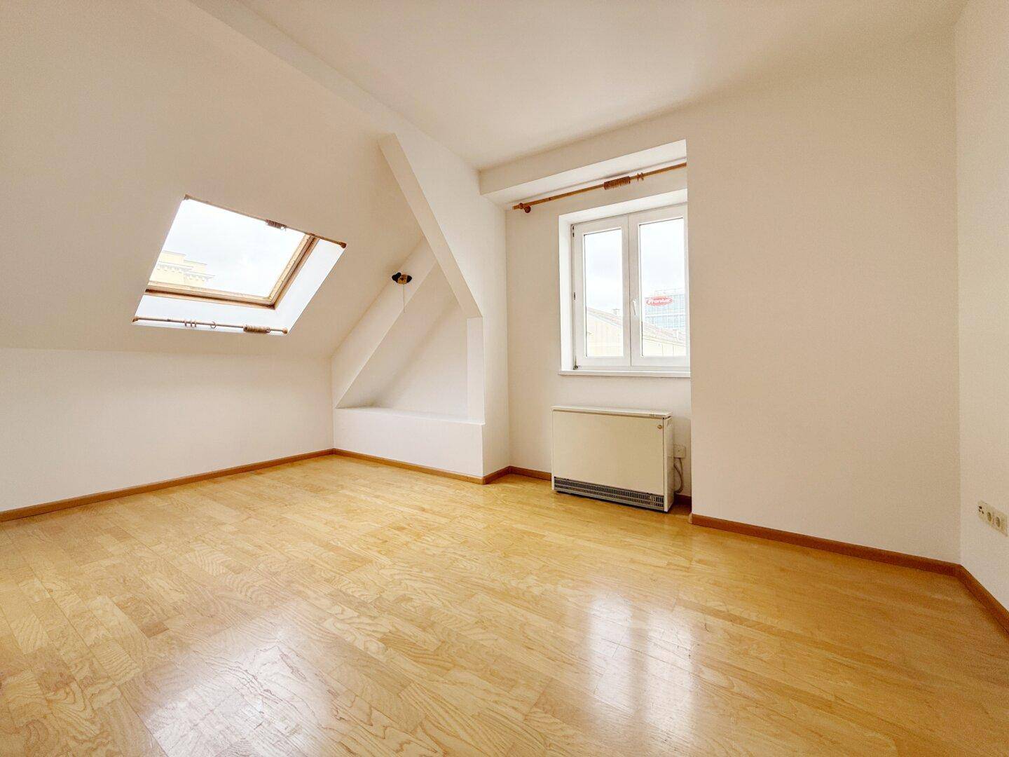Dachraum mit Parkettboden, Dachschräge und einem Dachfenster für Helligkeit.