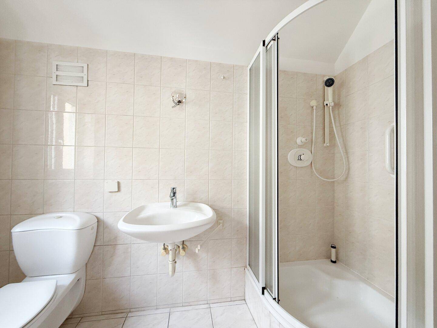 Badezimmer mit Duschkabine, Waschbecken und Toilette in hellen Fliesen.