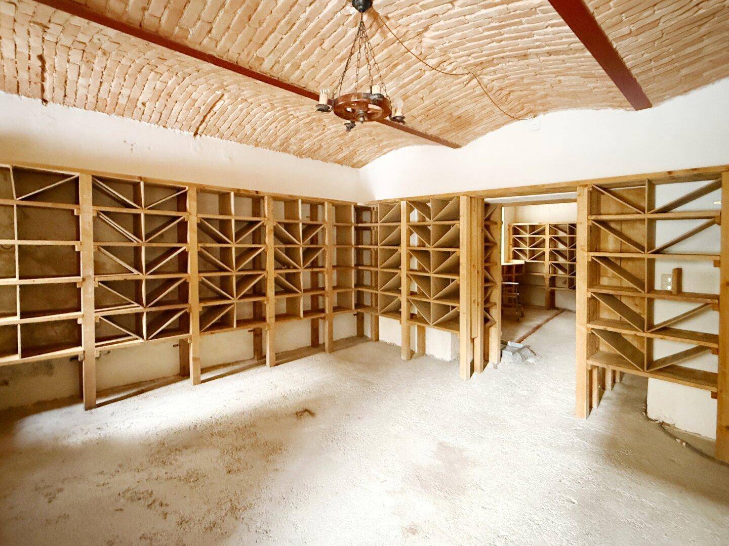 Historischer Weinkeller mit Ziegelgewölbedecke und Holzregalen für Flaschen.