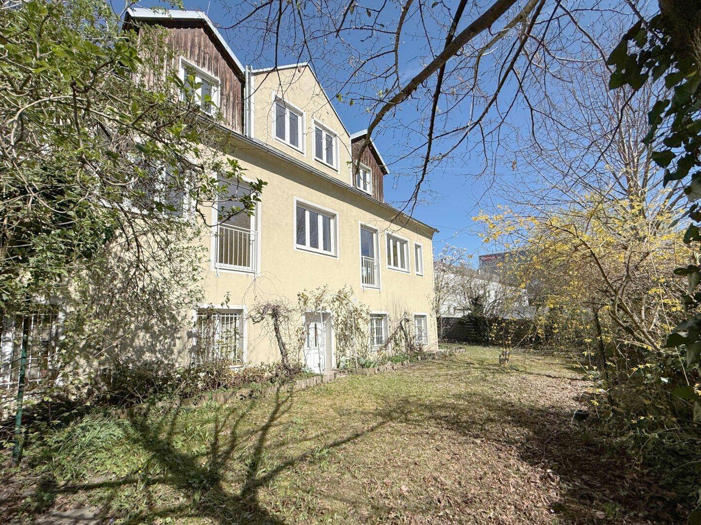 Gartenansicht des Gebäudes mit viel Grün und sonnigen Bereichen.
