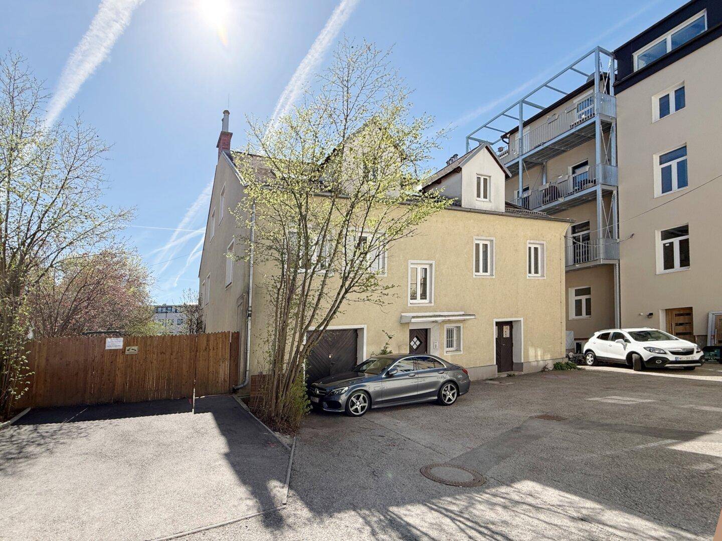 Außenansicht des Gebäudes mit Parkplätzen und angrenzendem Neubau.