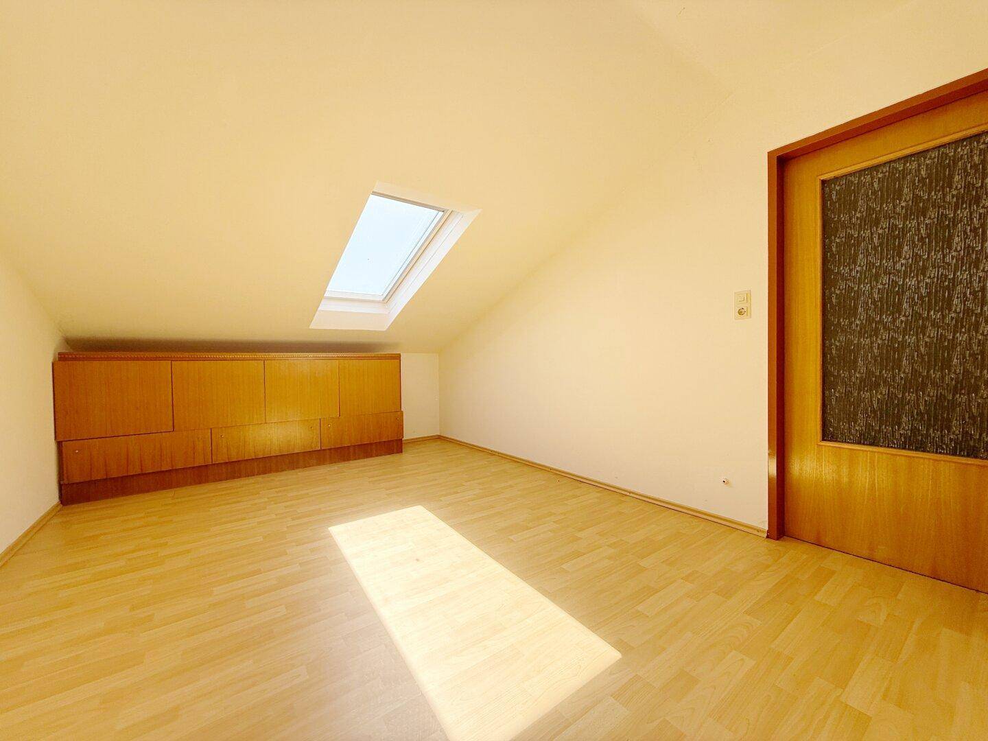 Leeres Zimmer im Dachgeschoss mit Parkettboden, Dachfenster und Einbauschränken.