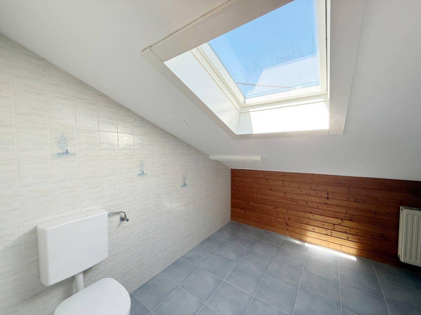 WC-Bereich im Dachgeschoss mit Dachfenster, Fliesen und Holzverkleidung.