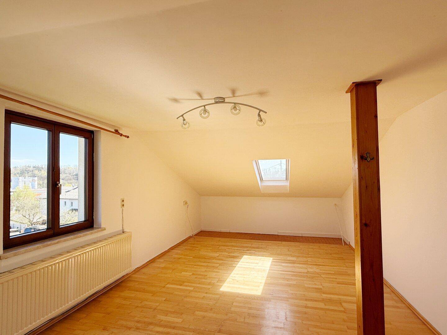 Lichtdurchfluteter Dachgeschossraum mit Parkettboden, Dachfenster und weitem Blick.