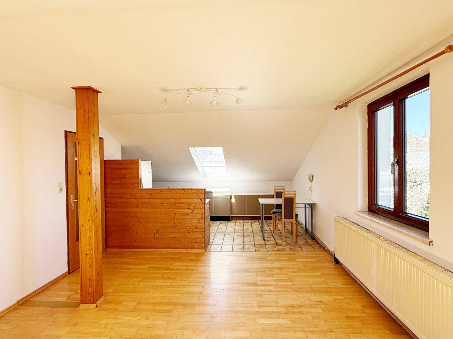 Offener Wohnbereich im Dachgeschoss mit Holzbalken, Parkettboden und Dachfenster.