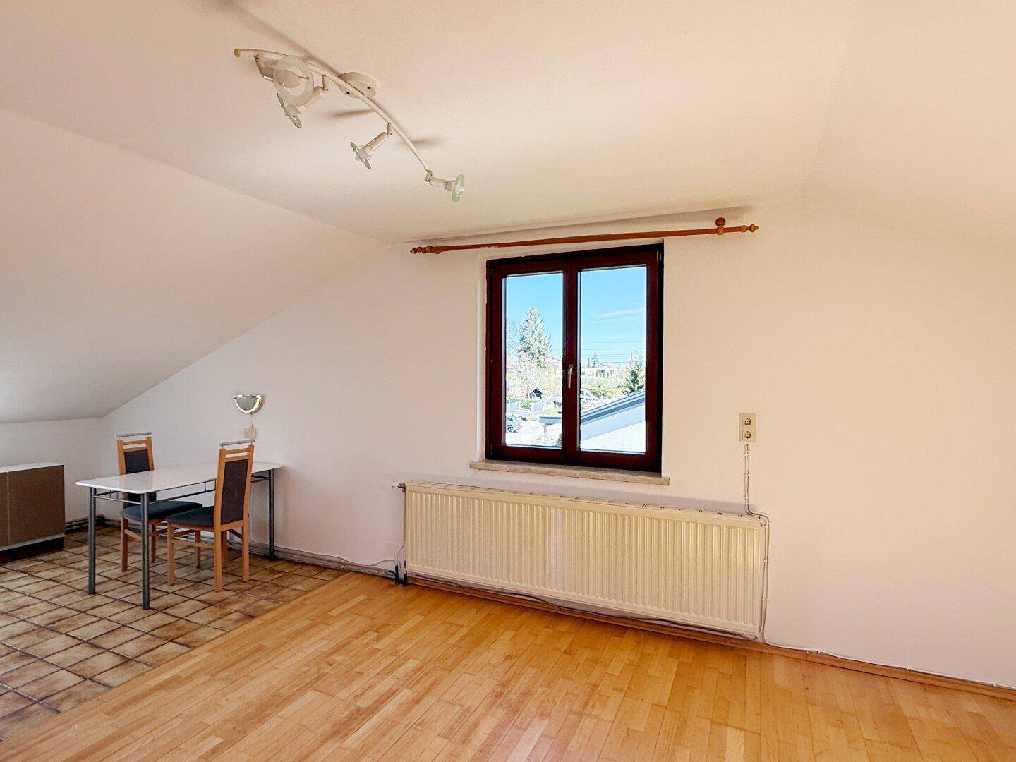 Heller Dachgeschossraum mit Esstisch, Parkettboden und Fenster mit Ausblick.